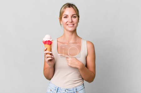 Téléchargez les photos : Caucasian blonde woman smiling cheerfully, feeling happy and pointing to the side. ice cream concept - en image libre de droit