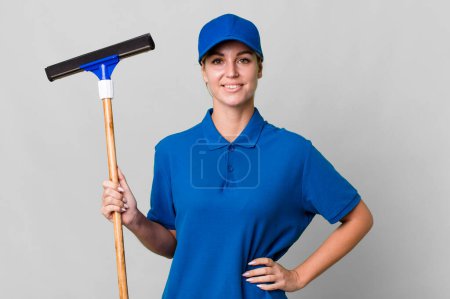Photo for Caucasian blonde woman smiling happily with a hand on hip and confident. windows washer concept - Royalty Free Image