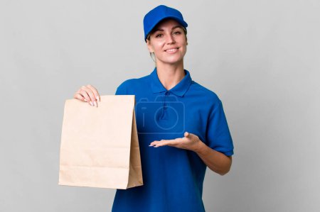 Téléchargez les photos : Caucasian blonde woman smiling cheerfully, feeling happy and showing a concept. paper bag delivery concept - en image libre de droit