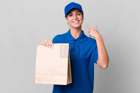 Photo for Caucasian blonde woman smiling confidently pointing to own broad smile. paper bag delivery concept - Royalty Free Image