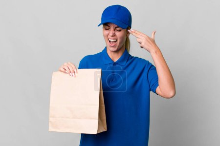 Foto de Caucasian blonde woman looking unhappy and stressed, suicide gesture making gun sign. paper bag delivery concept - Imagen libre de derechos