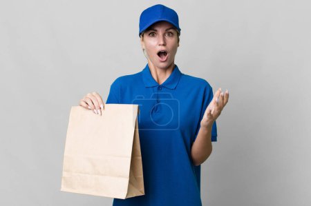 Photo for Caucasian blonde woman feeling extremely shocked and surprised. paper bag delivery concept - Royalty Free Image