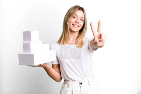 Photo for Young pretty woman smiling and looking happy, gesturing victory or peace. blank white boxes concept - Royalty Free Image