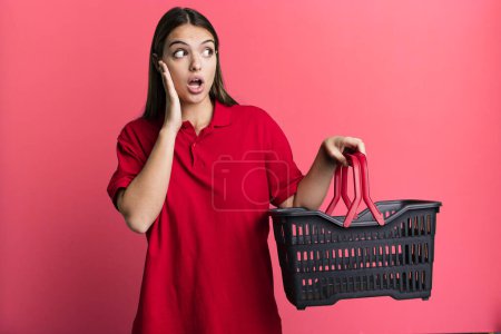 Photo for Young pretty woman feeling happy, excited and surprised. empty shopping basket concept - Royalty Free Image