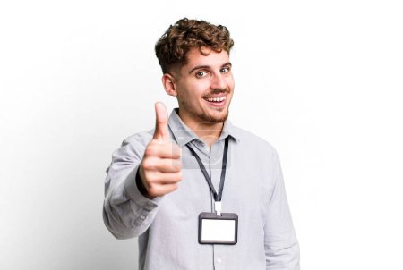 Foto de Young adult caucasian man feeling proud,smiling positively with thumbs up. blank accreditation pass card id concept - Imagen libre de derechos