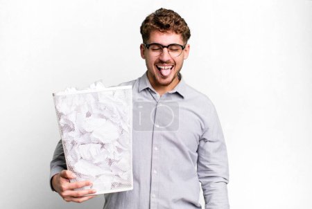 Foto de Young adult caucasian man with cheerful and rebellious attitude, joking and sticking tongue out with a paper balls trash concept - Imagen libre de derechos