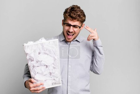 Photo for Young adult caucasian man looking unhappy and stressed, suicide gesture making gun sign with a paper balls trash concept - Royalty Free Image