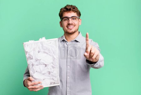Foto de Young adult caucasian man smiling proudly and confidently making number one with a paper balls trash concept - Imagen libre de derechos