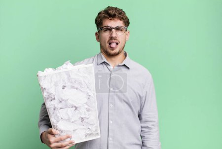 Photo for Young adult caucasian man feeling disgusted and irritated and tongue out with a paper balls trash concept - Royalty Free Image