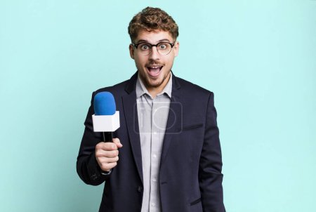 Photo for Young adult caucasian man looking very shocked or surprised. journalist or presenter with a microphone - Royalty Free Image