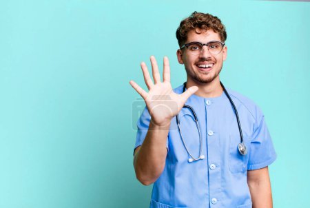 Téléchargez les photos : Young adult caucasian man smiling and looking friendly, showing number five. nurse concept - en image libre de droit
