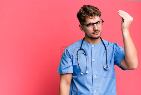 Téléchargez les photos : Young adult caucasian man making capice or money gesture, telling you to pay. nurse concept - en image libre de droit