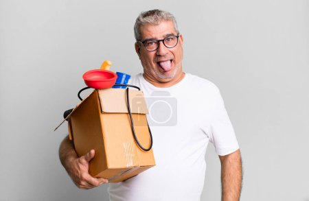 Foto de Hombre mayor de mediana edad con actitud alegre y rebelde, bromeando y sacando la lengua. ama de llaves reparador con un concepto de caja de herramientas - Imagen libre de derechos