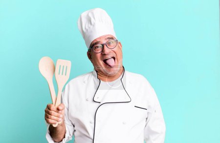 Foto de Hombre mayor de mediana edad con actitud alegre y rebelde, bromeando y sacando la lengua. chef de restaurante con un concepto de herramienta - Imagen libre de derechos