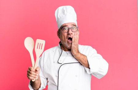Foto de Hombre mayor de mediana edad sintiéndose sorprendido y asustado. chef de restaurante con un concepto de herramienta - Imagen libre de derechos