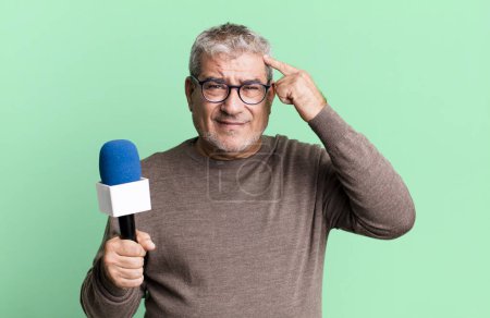 Foto de Hombre mayor de mediana edad sintiéndose confundido y perplejo, mostrando que estás loco. periodista o presentador de televisión con un micro - Imagen libre de derechos
