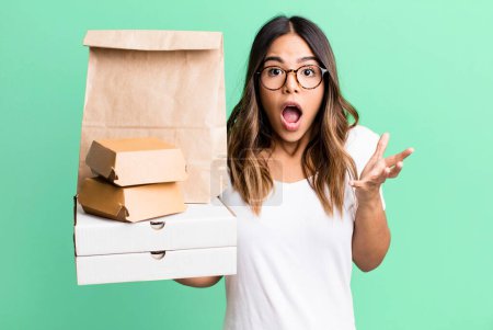 Photo for Hispanic pretty woman amazed, shocked and astonished with an unbelievable surprise. delivery and take away fast food concept - Royalty Free Image