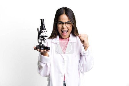 Photo for Hispanic pretty woman feeling shocked,laughing and celebrating success. scients student with a microscope - Royalty Free Image
