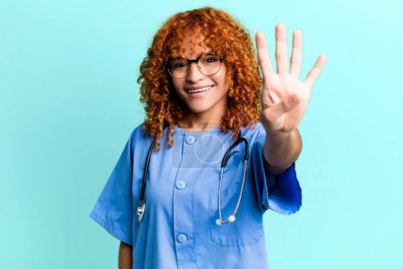 Téléchargez les photos : Cheveux roux jolie femme souriante et sympathique, montrant le numéro quatre. concept d'infirmière - en image libre de droit