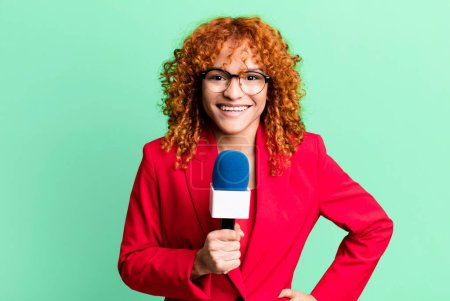 Photo for Red hair pretty woman smiling happily with a hand on hip and confident. journalist and presenter concept - Royalty Free Image