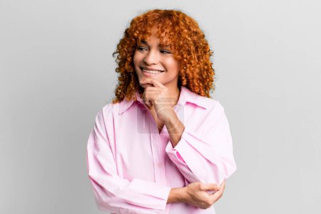 Photo for Redhair pretty woman smiling with a happy, confident expression with hand on chin, wondering and looking to the side - Royalty Free Image