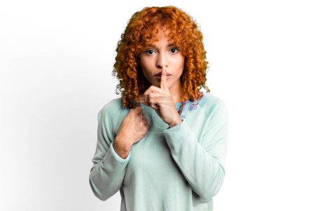 Photo for Redhair pretty woman looking serious and cross with finger pressed to lips demanding silence or quiet, keeping a secret - Royalty Free Image