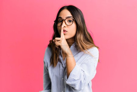 Photo for Hispanic pretty woman asking for silence and quiet, gesturing with finger in front of mouth, saying shh or keeping a secret - Royalty Free Image