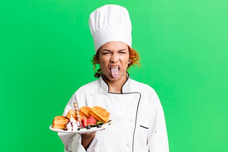 Foto de Pelo rojo bastante chef mujer cocina gofres - Imagen libre de derechos