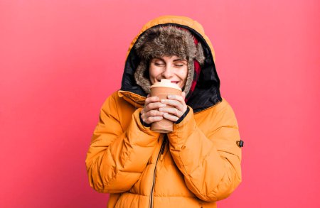 Photo for Young adult pretty woman wearing anorak and winter hat and holding a take away coffee - Royalty Free Image