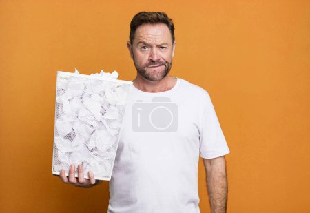 Photo for Middle age man looking puzzled and confused. paper balls trash basket - Royalty Free Image