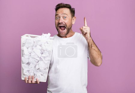 Téléchargez les photos : Middle age man feeling like a happy and excited genius after realizing an idea. paper balls trash basket - en image libre de droit