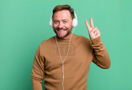 Téléchargez les photos : Middle age man smiling and looking friendly, showing number two. listening music with a headphones - en image libre de droit