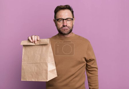 Foto de Middle age man feeling sad and whiney with an unhappy look and crying. take away paper bag - Imagen libre de derechos