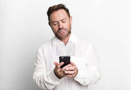 Téléchargez les photos : Homme d'âge moyen en utilisant son concept de coach sportif smartphone avec un ballon de football - en image libre de droit