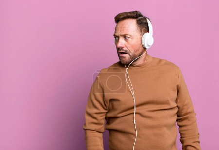 Foto de Hombre de mediana edad escuchando música con sus auriculares concepto de entrenador deportivo con una pelota de fútbol - Imagen libre de derechos