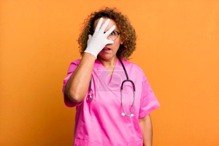 Photo for Pretty middle age woman looking shocked, scared or terrified, covering face with hand. nurse concept - Royalty Free Image