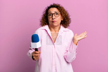 Foto de Pretty middle age woman feeling puzzled and confused and doubting. tv presenter with a microphone concept - Imagen libre de derechos