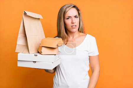 Foto de Bonita mujer rubia sintiéndose perpleja y confundida. entrega comida para llevar concepto de paquetes - Imagen libre de derechos