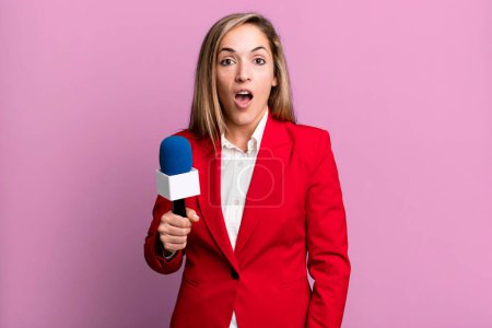 Photo for Pretty blonde woman looking very shocked or surprised. presenter with a microphone concept - Royalty Free Image