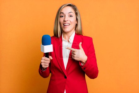 Foto de Pretty blonde woman looking excited and surprised pointing to the side. presenter with a microphone concept - Imagen libre de derechos