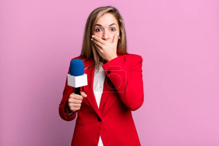 Foto de Bonita mujer rubia cubriendo la boca con las manos con un shock. presentador con un concepto de micrófono - Imagen libre de derechos
