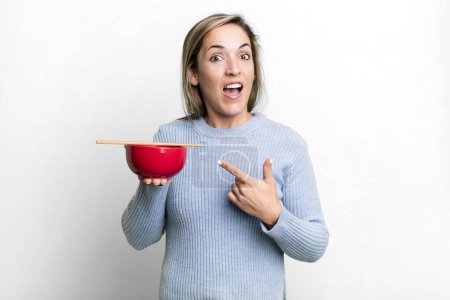 Photo for Pretty blonde woman looking excited and surprised pointing to the side. japanese noodles concept - Royalty Free Image