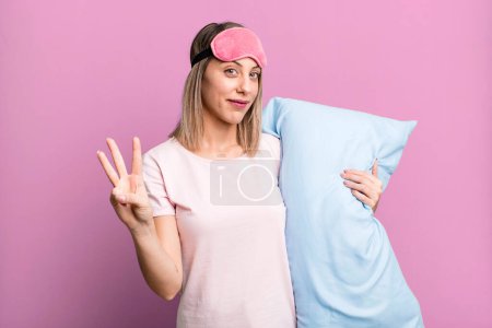 Foto de Pretty blonde woman smiling and looking friendly, showing number three. pajamas and nightwear concept - Imagen libre de derechos