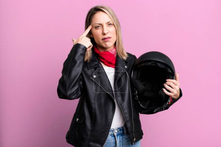 Photo for Pretty blonde woman feeling confused and puzzled, showing you are insane. motorbike rider and helmet concept - Royalty Free Image