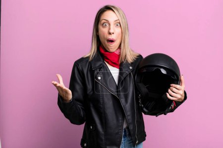 Foto de Mujer rubia bonita sorprendida, sorprendida y asombrada con una sorpresa increíble. motociclista y concepto de casco - Imagen libre de derechos