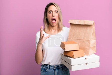 Photo for Pretty blonde woman screaming with hands up in the air. paper fast food take away packages - Royalty Free Image