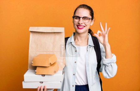 Foto de Pretty hispanic woman feeling happy, showing approval with okay gesture. delivery fast food take away concept - Imagen libre de derechos