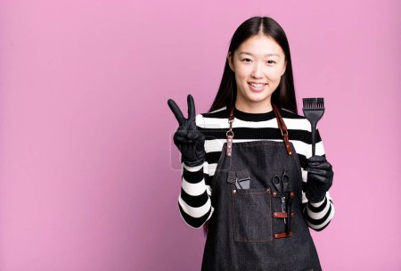 Photo for Pretty asian woman smiling and looking friendly, showing number two. barber concept - Royalty Free Image