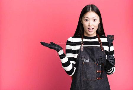 Photo for Pretty asian woman looking surprised and shocked, with jaw dropped holding an object. barber concept - Royalty Free Image