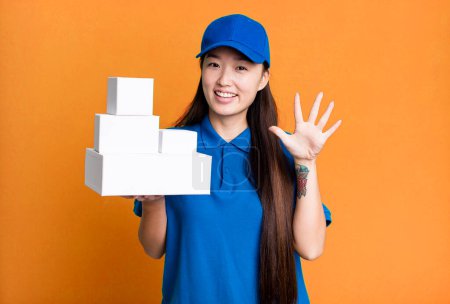 Téléchargez les photos : Pretty asian woman smiling and looking friendly, showing number five. delivery packages concept - en image libre de droit
